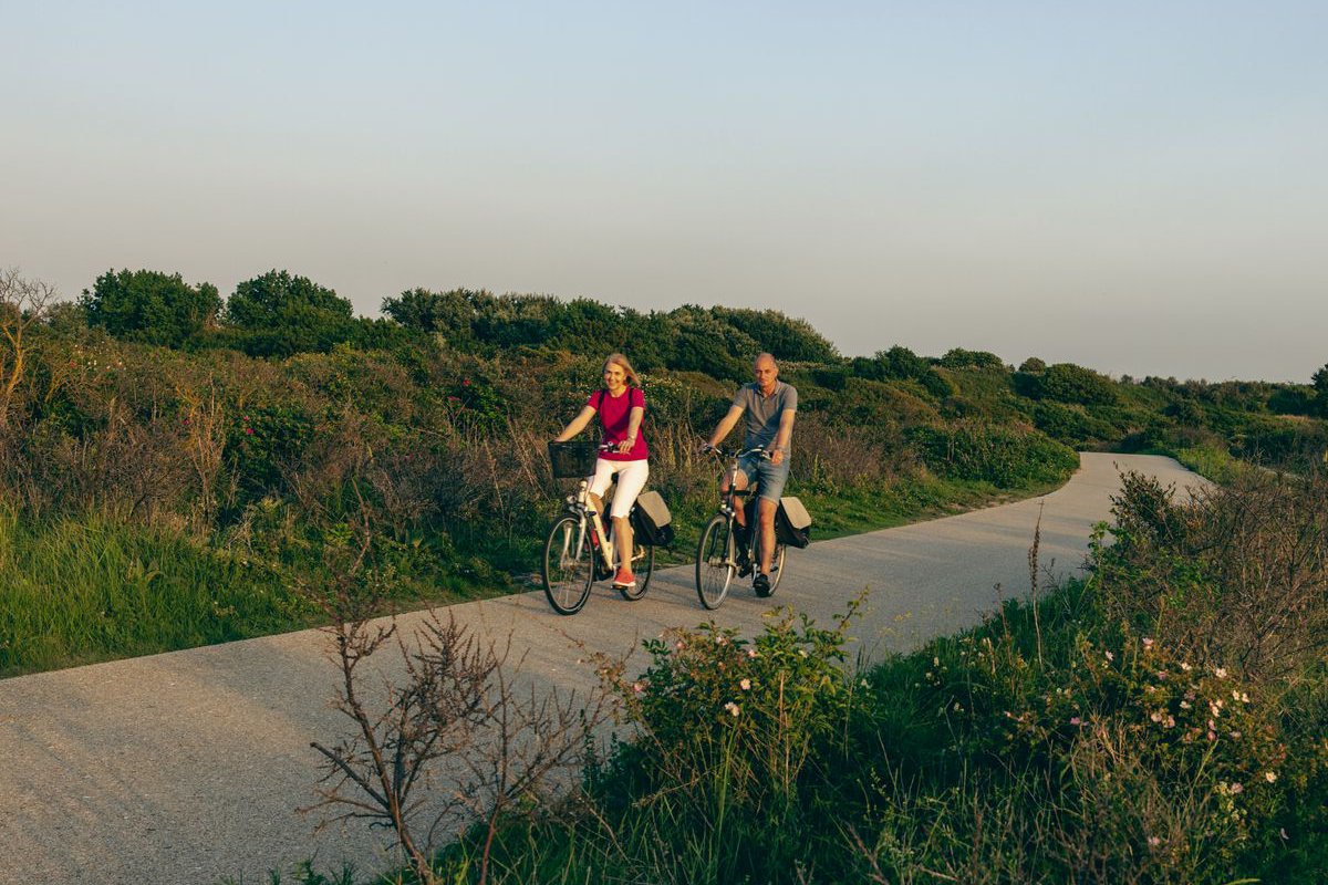 Couple riding bikes along a coastal dune path at golden hour