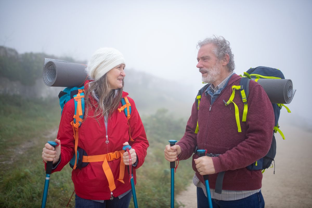 Couple with backpacks and trekking poles sharing a laugh on a misty trail